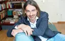 Richard David Precht sitzt lächelnd auf einem türkisfarbenen Sofa, im Hintergrund ein Bücherregal.