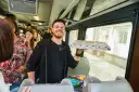 Uśmiechnięty mężczyzna z pizzą w ręku w pociągu relacji Kraków-Praga.