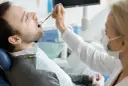 Pacjent u dentysty, zastanawia się, ile kosztuje wizyta u dentysty prywatnie. Lekarz bada jego zęby.