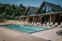 Basen z leżakami przy drewnianym hotelu w górach.