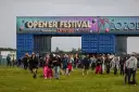 Tłum ludzi wchodzi na teren festiwalu. Nad nimi brama z napisem "OPEN'ER FESTIVAL". Kto będzie następny?