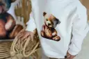 Biała bluza Moschino z uroczym misiem w stylu vintage. Dziecko trzyma się wiklinowego koszyka.
