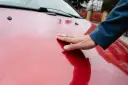 Dłoń dotyka błyszczącej, czerwonej maski samochodu.