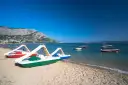 Plaża z łódkami i zjeżdżalniami, idealna na wakacje w camping Galeb. W tle góry i turkusowe morze.