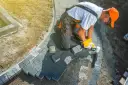 Brukar kostkę brukową, układając ją na piasku. Widać, ile kamienia pod kostkę jest potrzebne do stworzenia ścieżki.