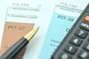 Dwa formularze podatkowe, PIT-38 i PIT-37, leżą obok siebie, gotowe do wypełnienia. Obok leży długopis i kalkulator.