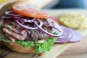 Soczysty burger z bekonem, pomidorem i czerwoną cebulą na desce.