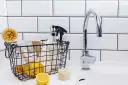 Kosz z cytrynami, szczotką i butelką octu obok kranu w łazience.