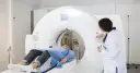 Pacjentka leży na stole tomografu, przygotowanie do tomografii z kontrastem. Lekarka obsługuje konsolę.