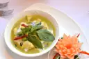 Zielone curry z kurczakiem, ozdobione bazylią i kwiatkiem z marchewki.
