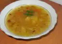 Prosta zupa cebulowa z ziemniakami, z kawałkami marchewki i natką pietruszki, podana w białej misce.