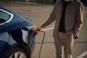 Mężczyzna podłącza ładowarkę do ciemnoniebieskiego samochodu elektrycznego. Zastanawiasz się, ile kosztuje ładowanie samochodu elektrycznego?