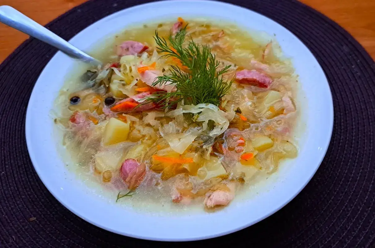 Syta zupa z kiszonej kapusty z ziemniakami i kiełbasą, ozdobiona koperkiem. Pyszne dania z kapusty na zimowe wieczory.