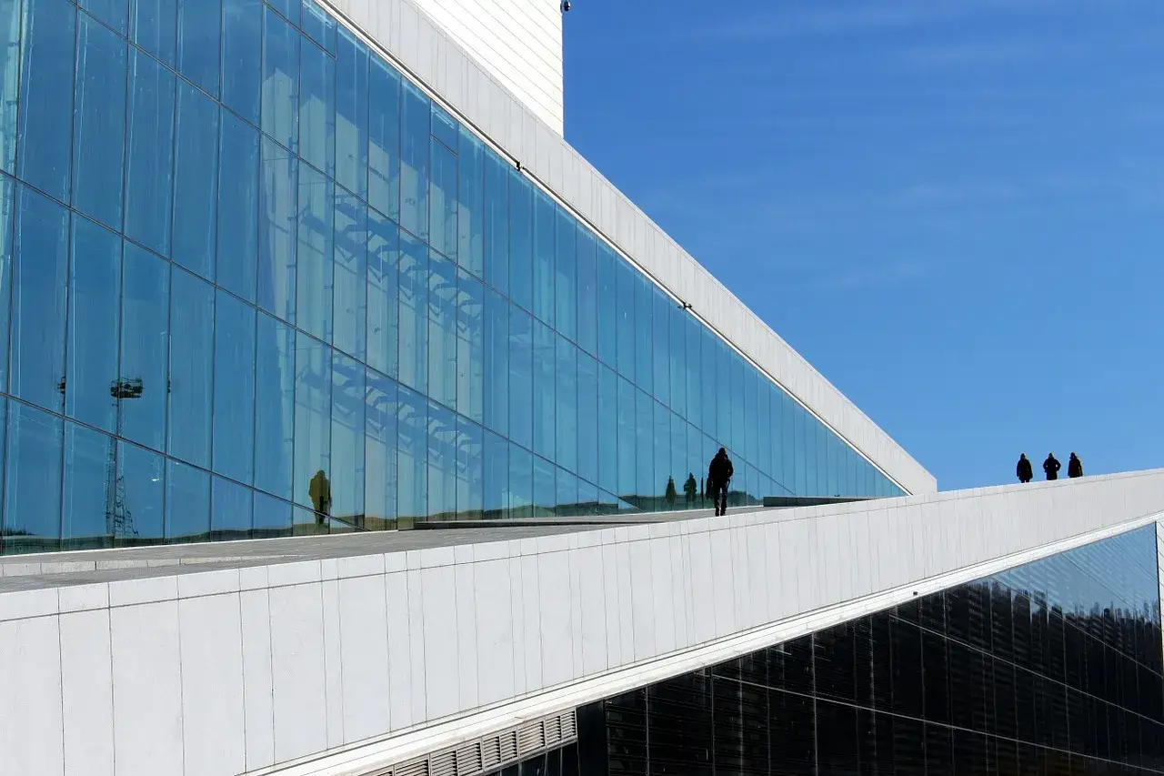 Nowoczesna architektura Uniwersytetu w Oslo z lustrzaną fasadą odbijającą niebo i ludzi.