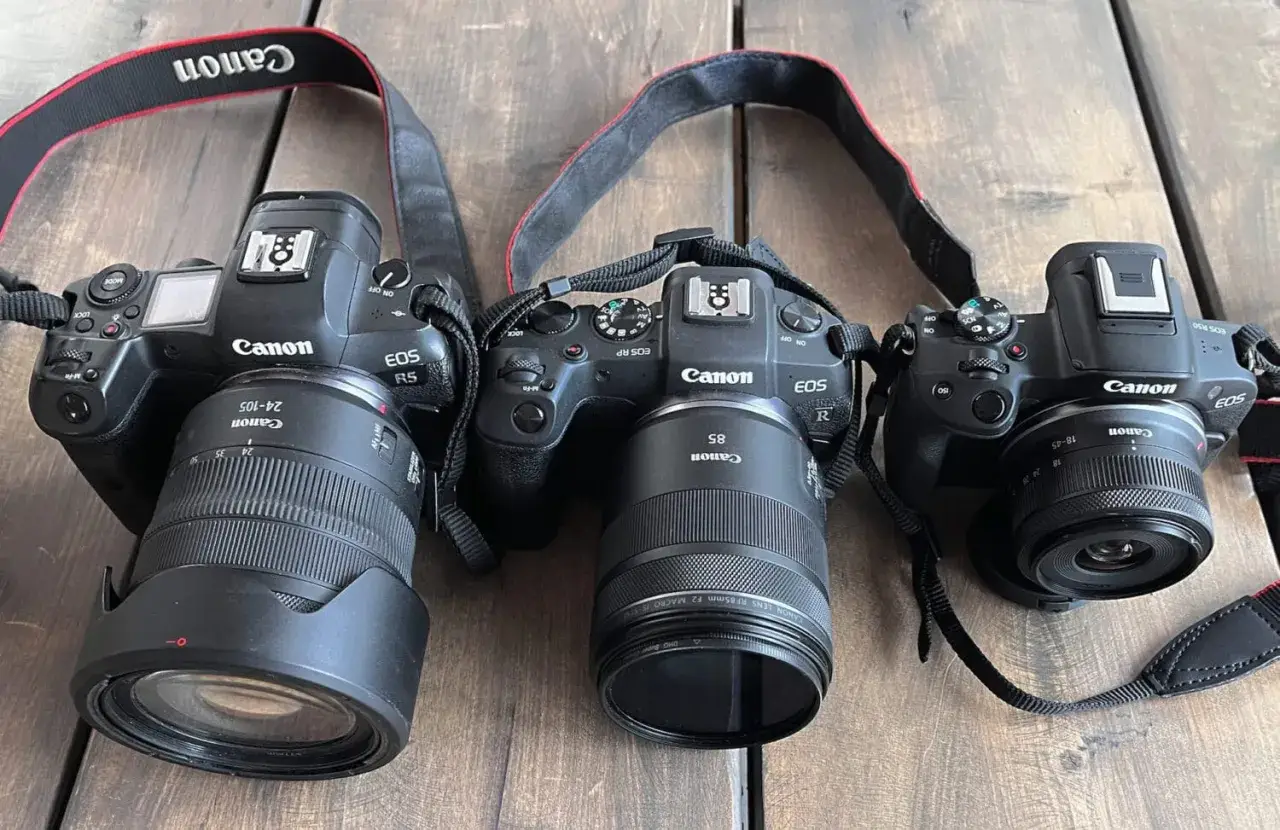 Trzy aparaty Canon EOS R, RP i R5 z obiektywami leżą obok siebie. Pełna klatka w całej okazałości.