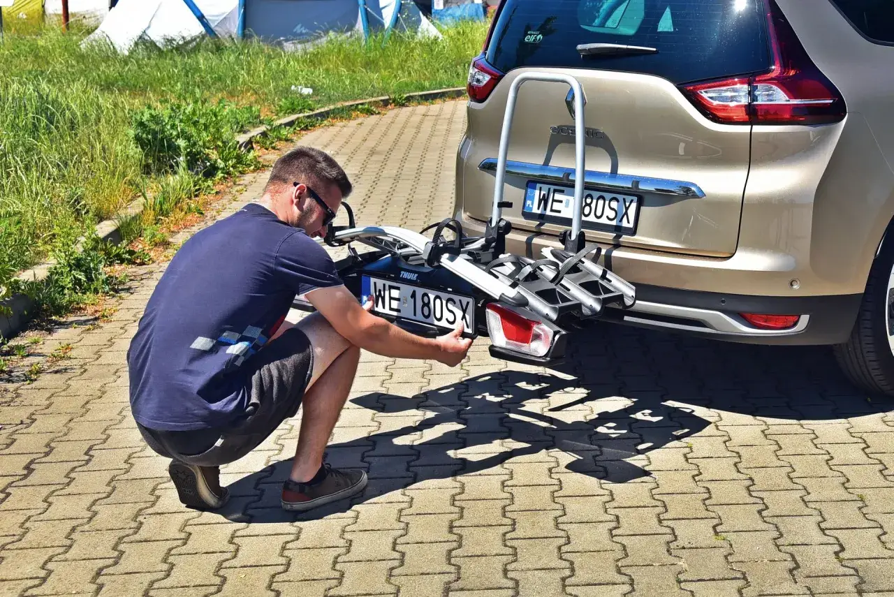 Mężczyzna montuje trzecią tablicę rejestracyjną WE 180SX na bagażniku rowerowym przy samochodzie.