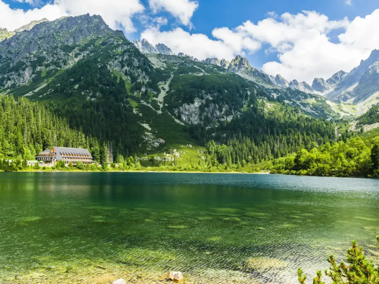 Zielone jeziora w Tatrach, otoczone lasem i majestatycznymi szczytami, z widocznym hotelem nad brzegiem.