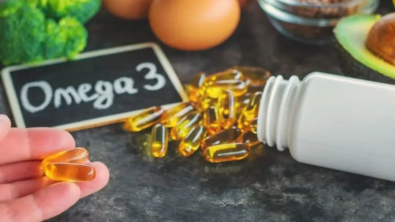 Dłoń trzyma kapsułki z kwasem omega 3. Obok leży buteleczka i tabliczka z napisem "Omega 3".