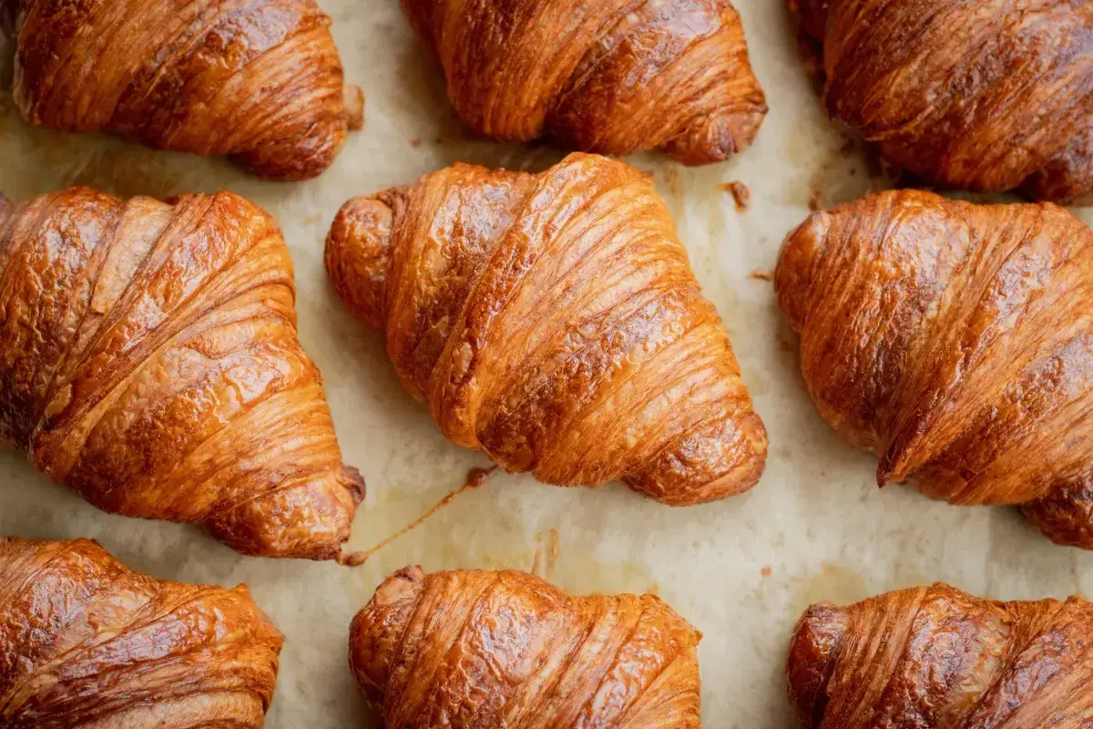 Złociste, chrupiące rogaliki ułożone na papierze do pieczenia. Idealne na śniadanie, choć warto pamiętać o ich kaloryczności – croissant kcal.