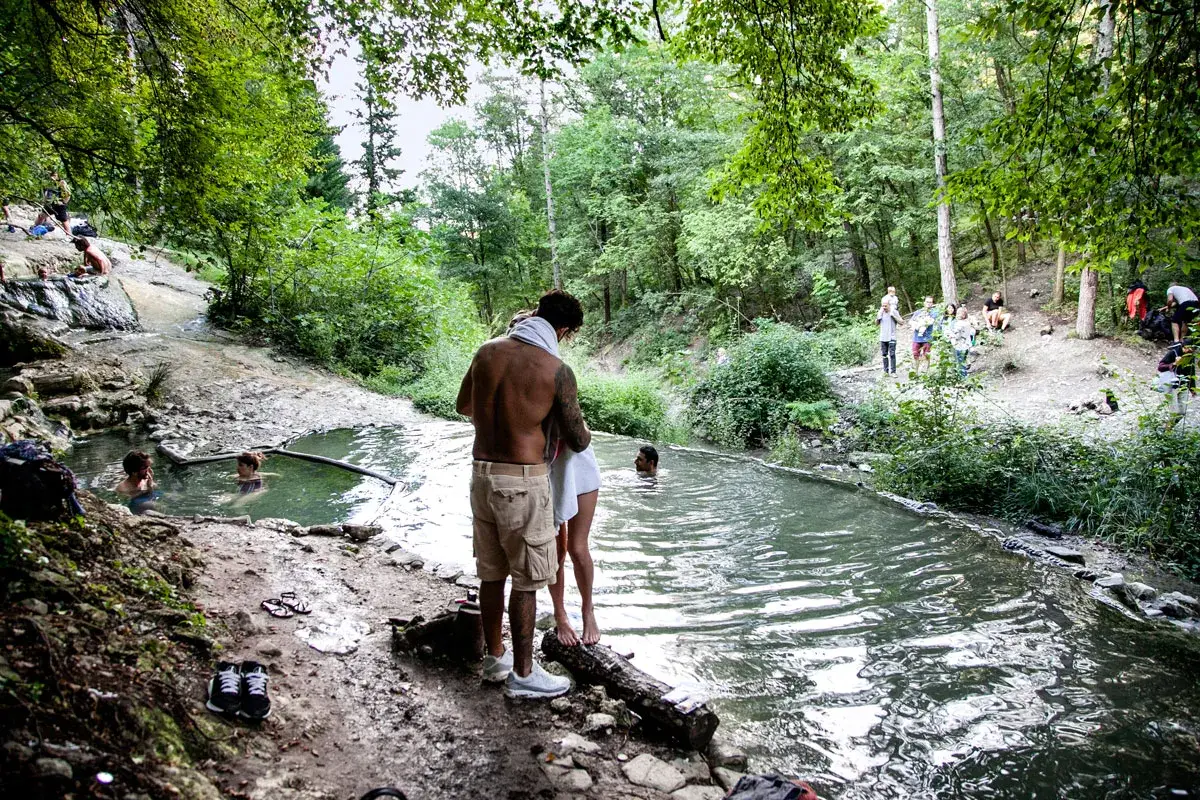 Persone si rilassano nelle acque termali dei Bagni di San Filippo, immersi nel verde di un bosco.