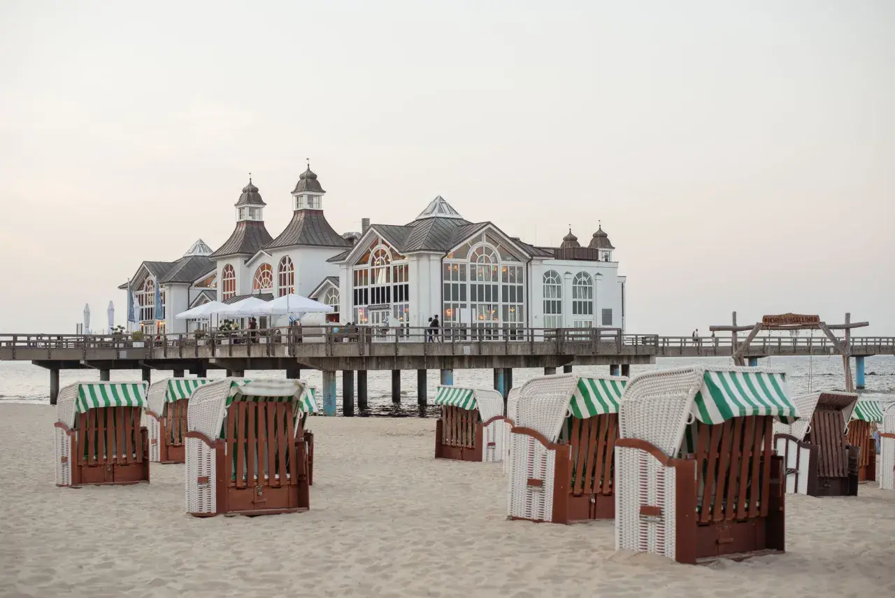 Plaża na wyspie Rugia z charakterystycznymi koszami plażowymi i molo prowadzącym do białego pawilonu.