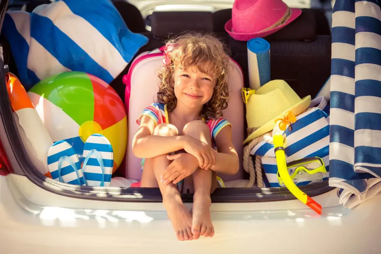 Niña sonriente rodeada de artículos de playa, lista para explorar nuevos sitios para ir con niños.