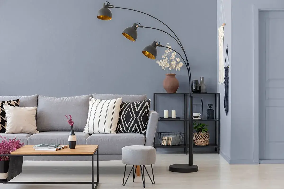 Przytulny salon z szarą kanapą, stolikiem kawowym i łukową lampą. Ciepły szary kolor ścian tworzy relaksującą atmosferę.