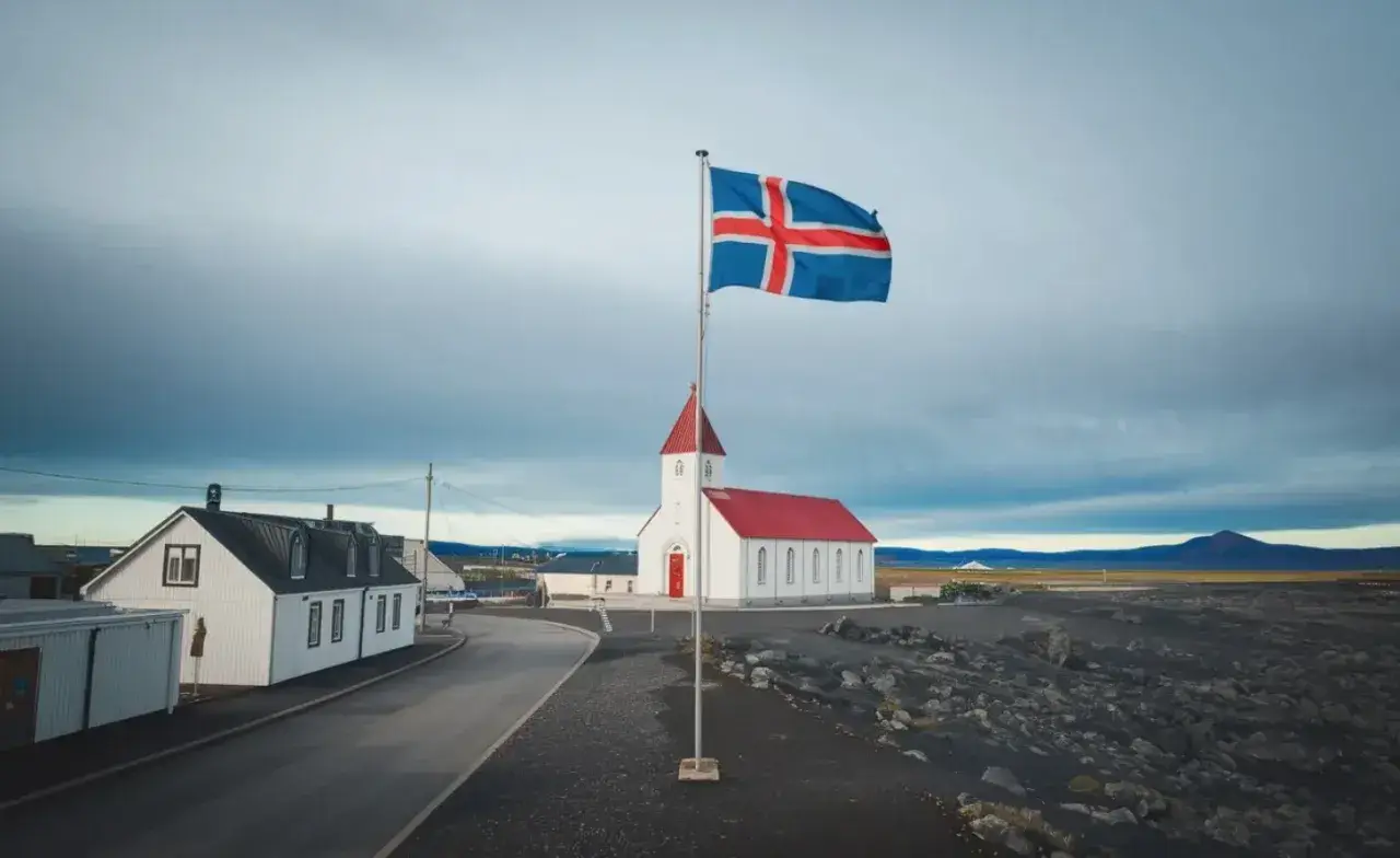 Islandia praca: biały kościół z czerwoną wieżą i flagą Islandii na tle pochmurnego nieba.