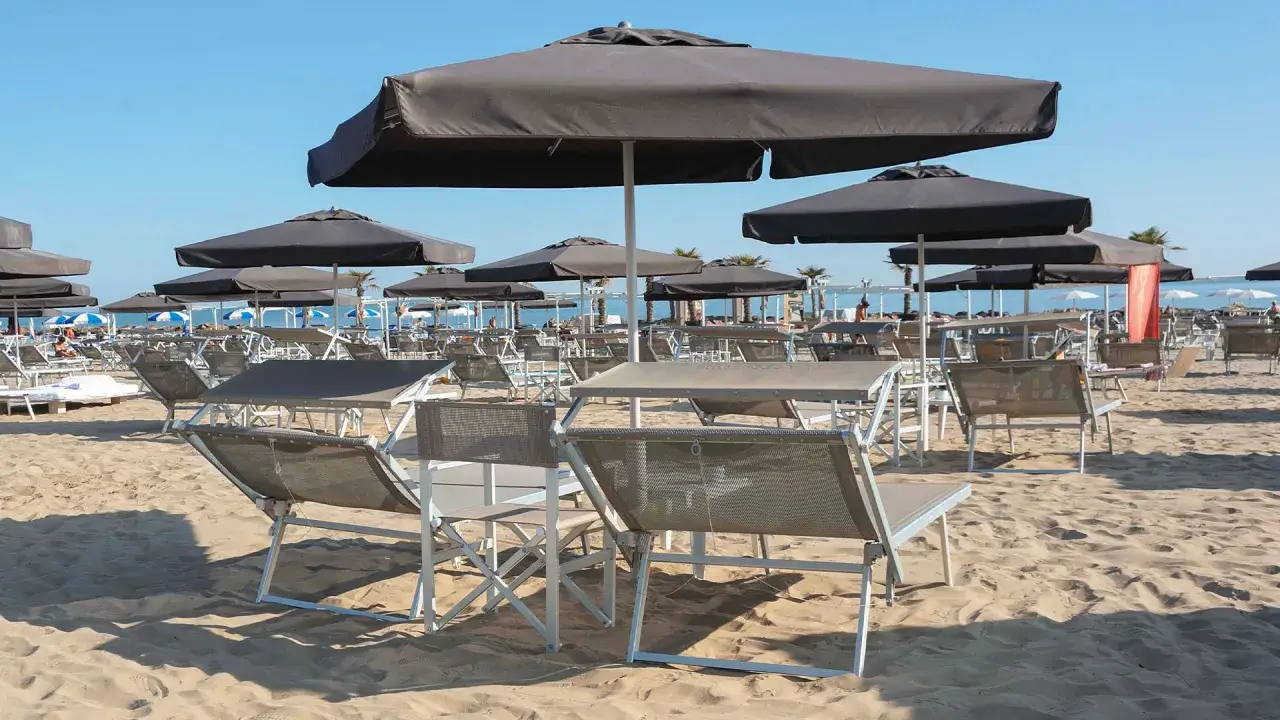 Lettini e ombrelloni scuri sulla sabbia dorata della **Baia degli Angeli Misano**, pronti per accogliere i bagnanti sotto il sole.