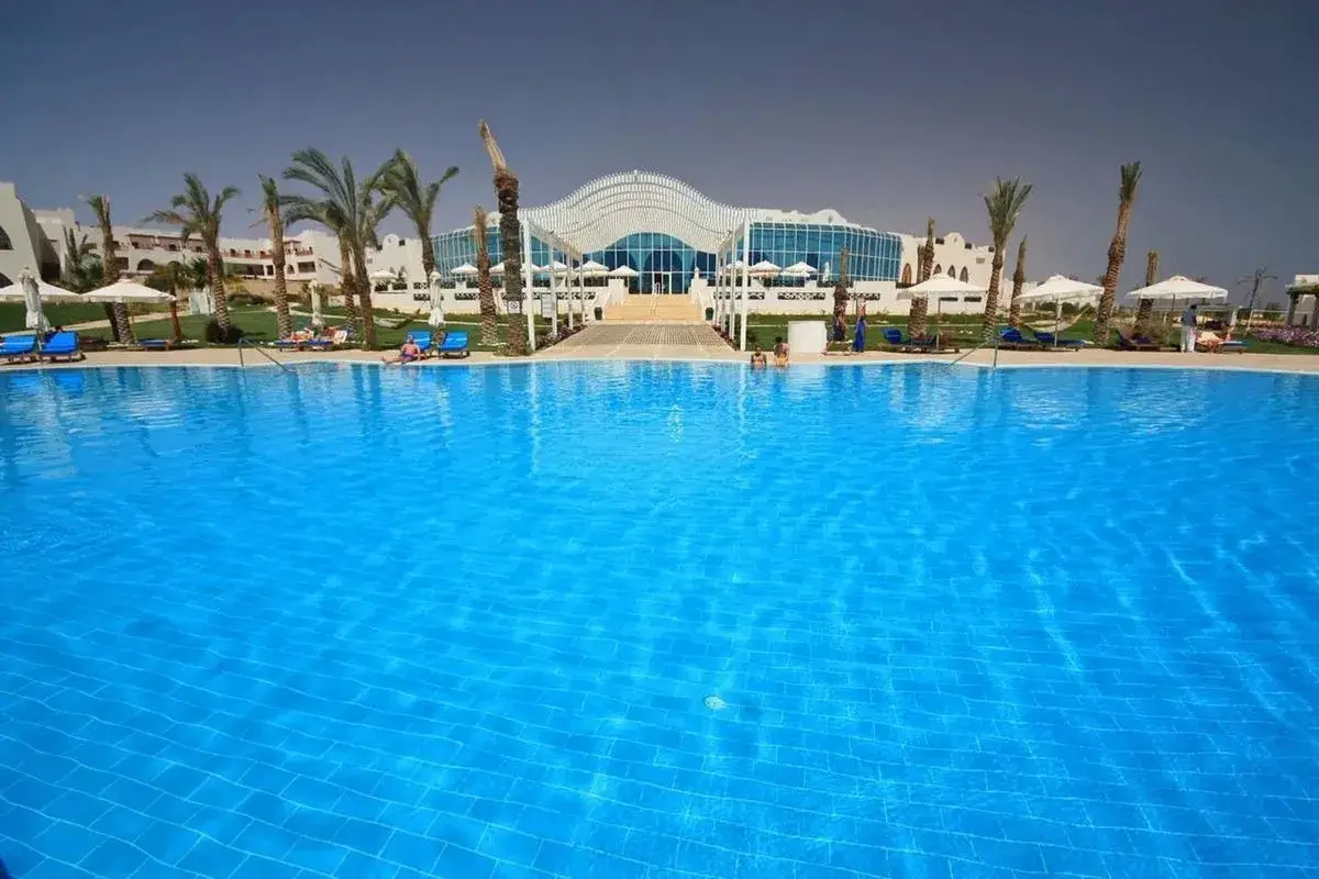 Basen w Hilton Marsa Alam Nubian Resort. Wiele osób odpoczywa na leżakach pod palmami.