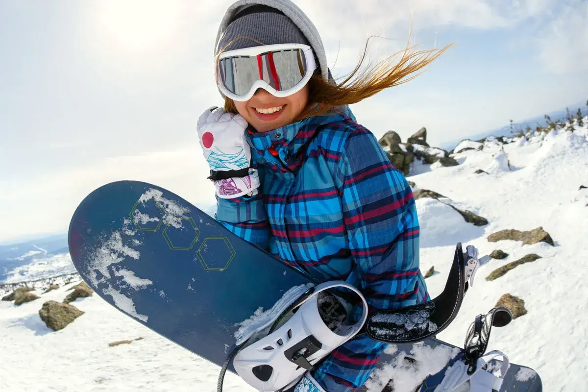 Uśmiechnięta snowboardzistka z deską, idealny dobór deski snowboardowej do wzrostu i wagi to klucz do zabawy na stoku.