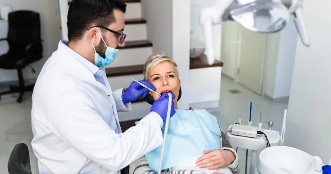 Dentysta wykonuje piaskowanie zębów u pacjentki, która siedzi na fotelu dentystycznym.