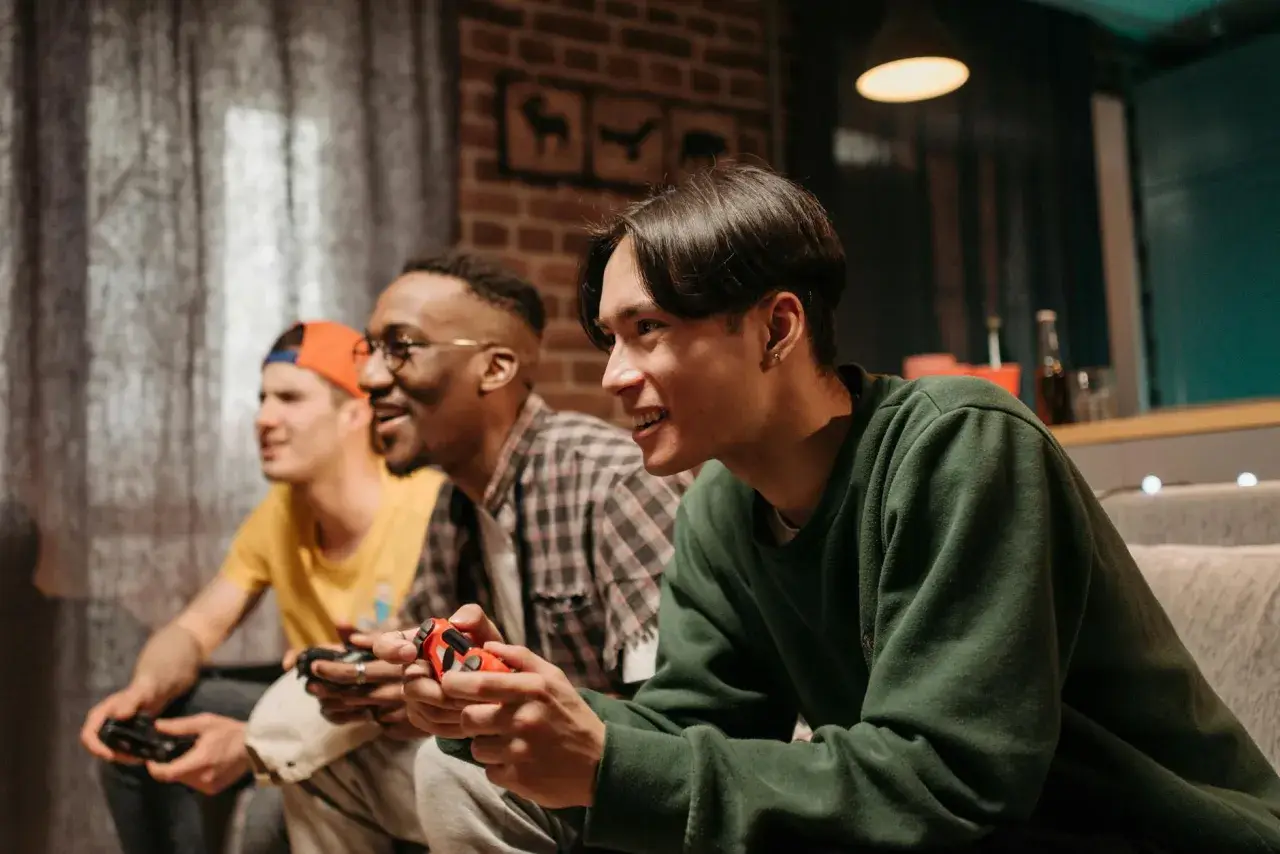 Trzech przyjaciół gra w darmowe gry na PS4, śmiejąc się i rywalizując.