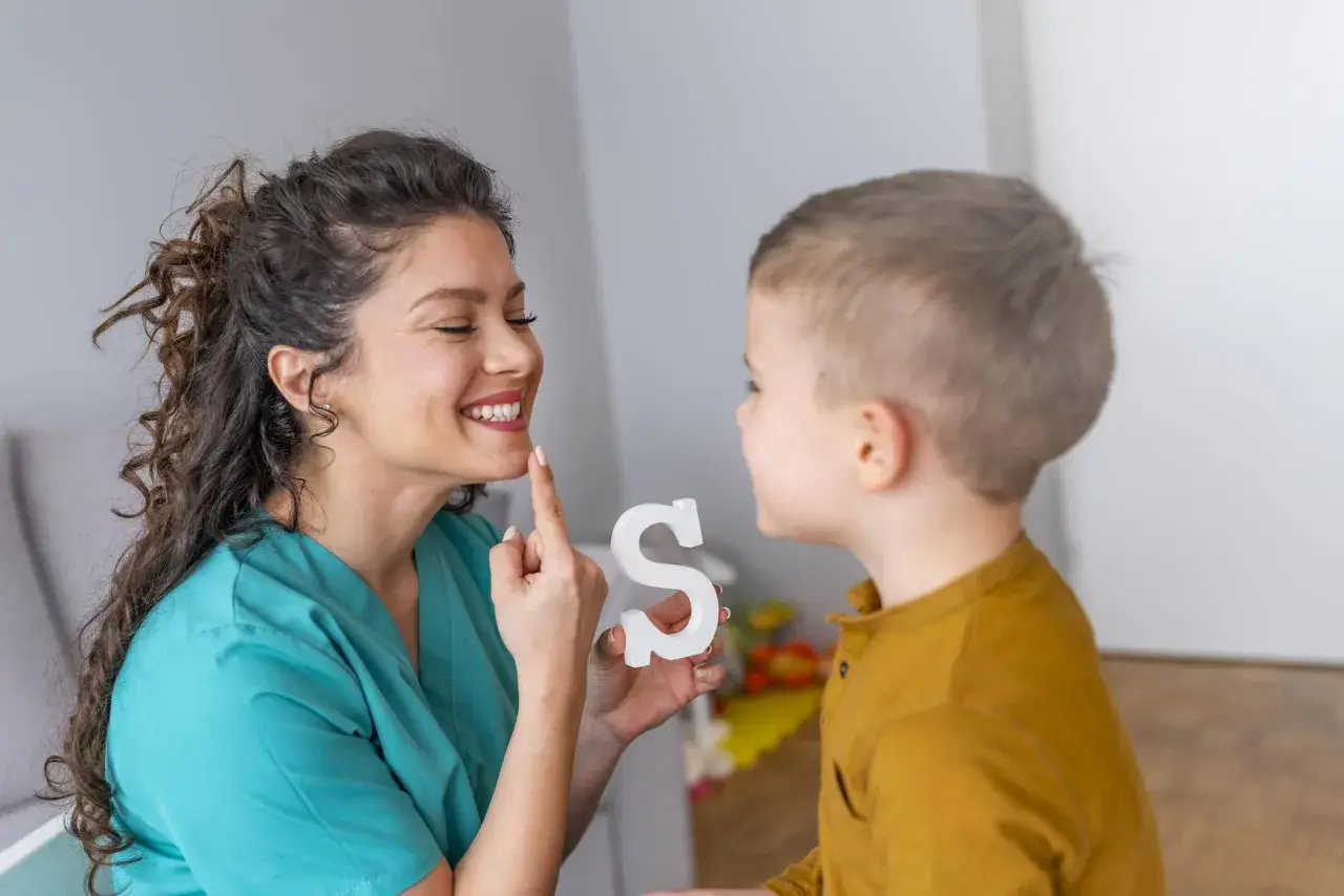 Logopeda pomaga dziecku z dyslalią ćwiczyć wymowę litery "S", używając białej literki.
