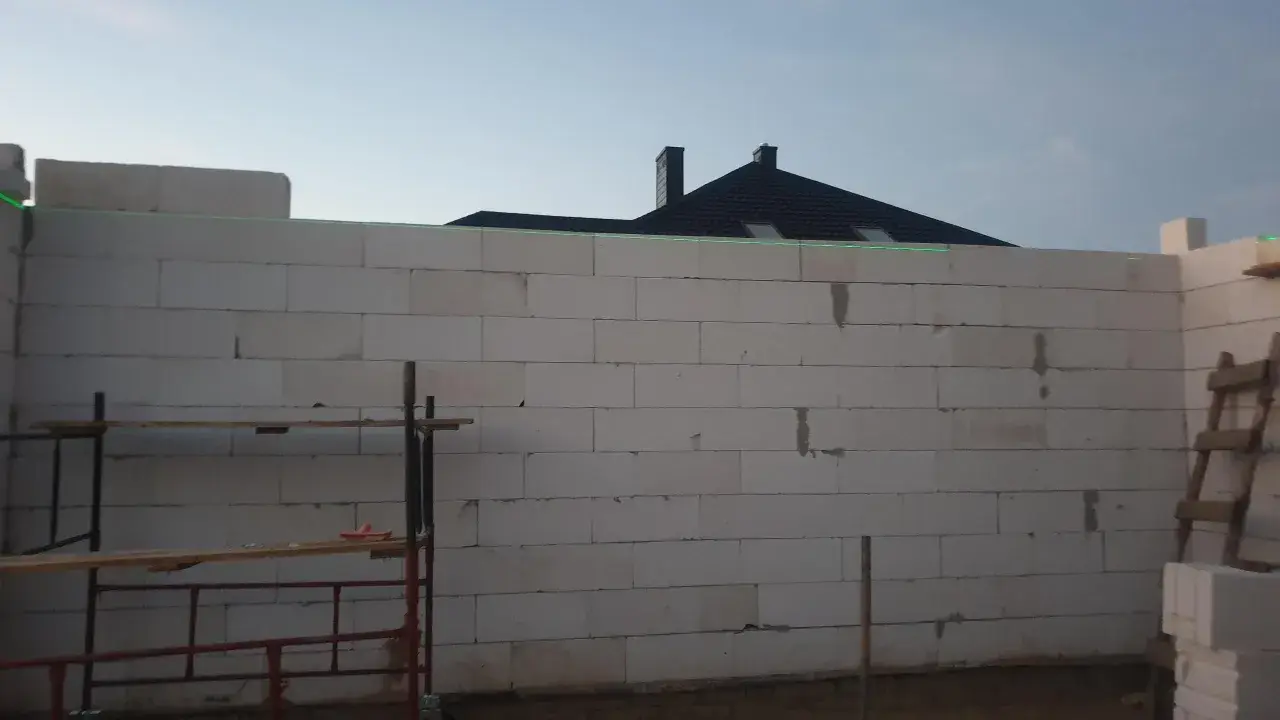 Budowa domu z bloczków, zielona linia laserowa wyznacza poziom. To dobry pomysł na krzywe ściany, jeśli chcesz uzyskać ciekawy efekt architektoniczny.