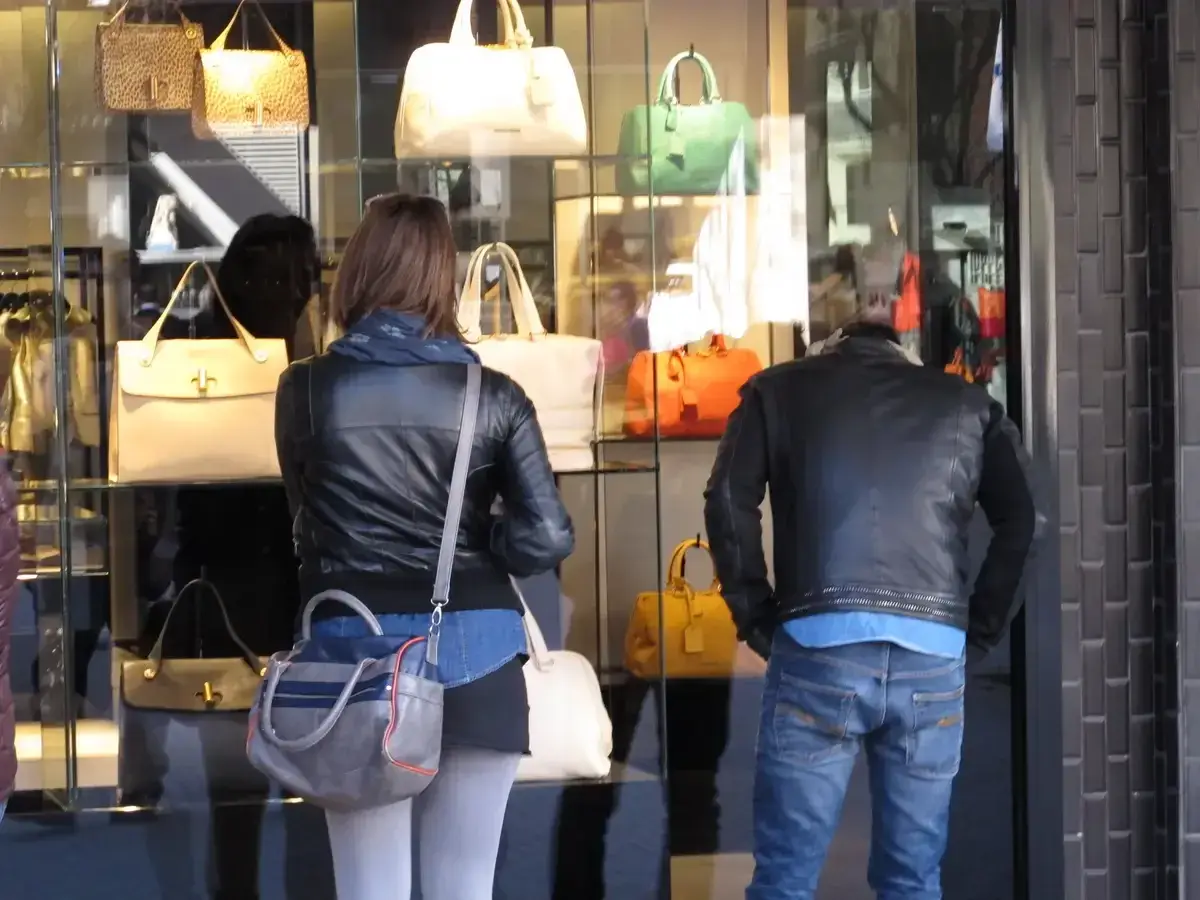 Coppia osserva vetrina di borse Benetton a Riccione. Lei con giacca in pelle, lui con giubbotto.