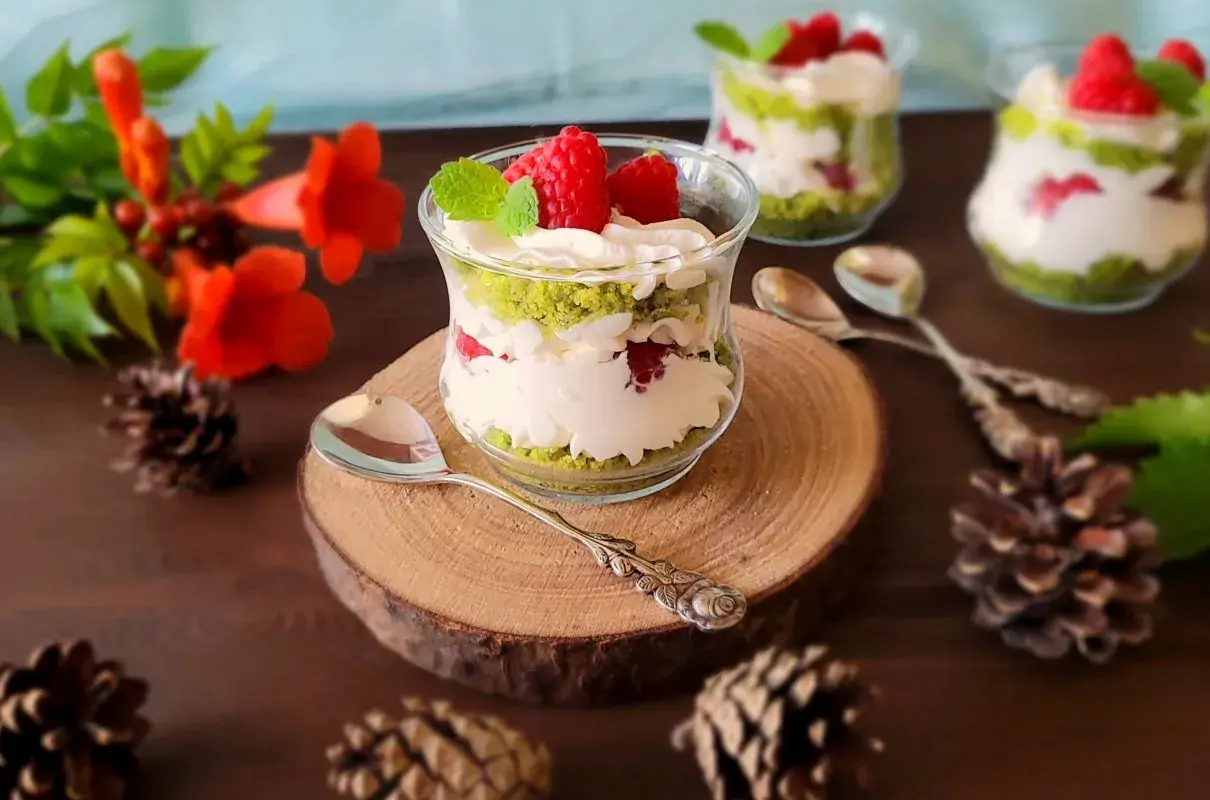 Pyszne ciasto leśny mech na dużą blachę z serkiem mascarpone, podane w szklanych pucharkach, ozdobione malinami i miętą.