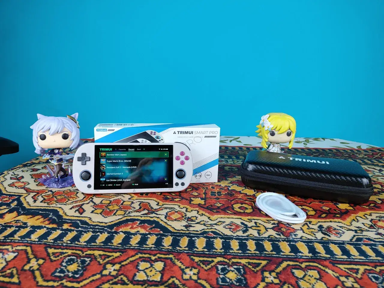 Biały handheld Trimui Smart Pro z grami, figurki Funko Pop i etui na konsolę.