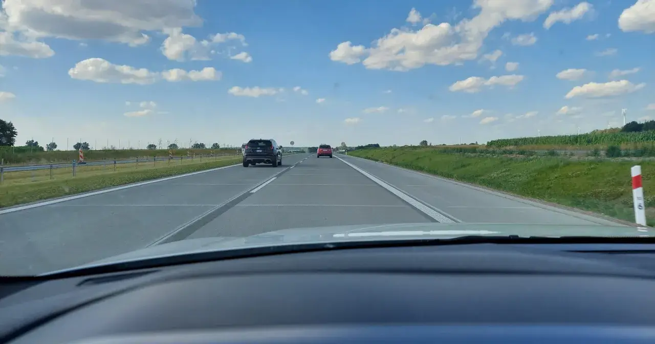 Jadąc na S7, widzimy pola i chmury. Samochody poruszają się po pustej drodze.