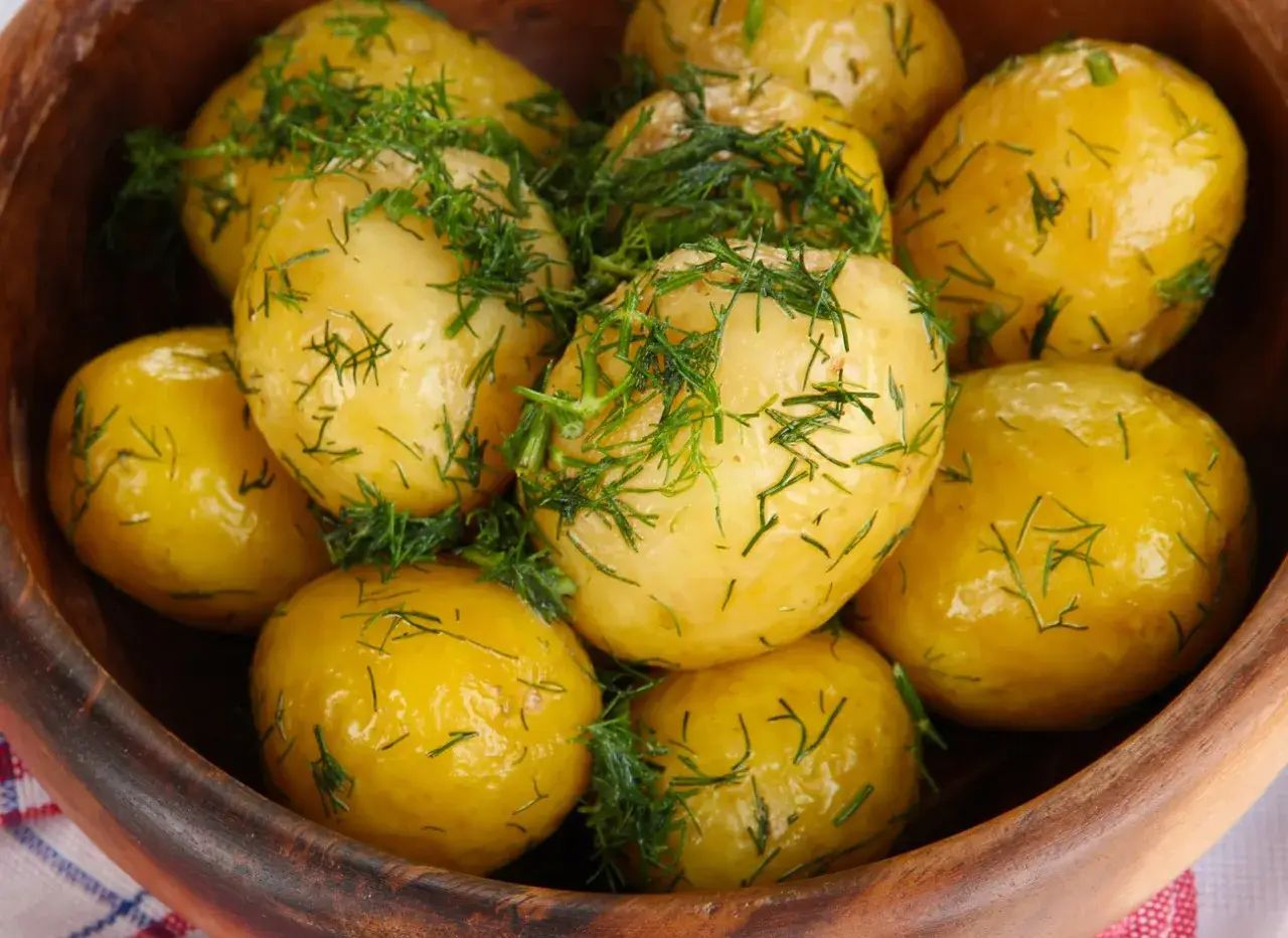 Ziemniaki gotowane w drewnianej misce, posypane świeżym koperkiem. Aromatyczne i apetyczne danie.