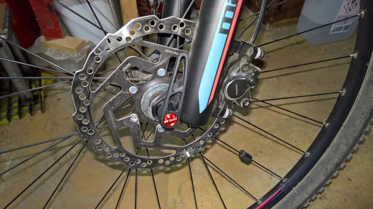 Hamulec tarczowy roweru z mocowaniem **center lock**. Widoczna tarcza hamulcowa Shimano, zacisk i szybkozamykacz DT Swiss.
