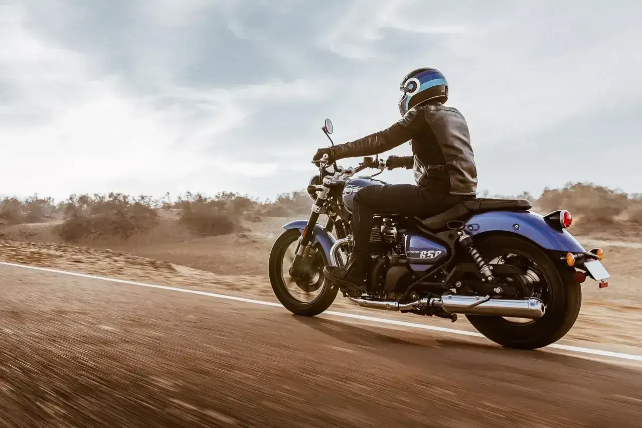 Motocyklista w skórzanej kurtce pędzi na niebieskim **super meteor 650** przez pustynny krajobraz.