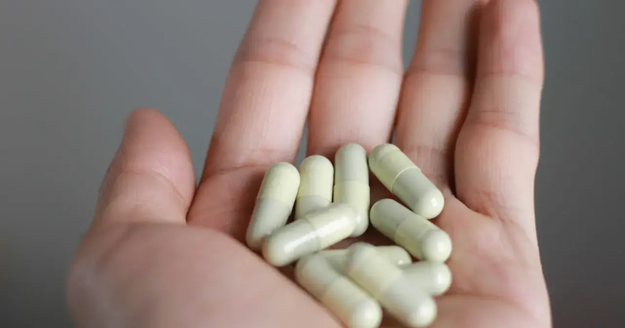Dłoń trzyma garść białych kapsułek. Warto sprawdzić witamina K przeciwwskazania przed ich przyjęciem.