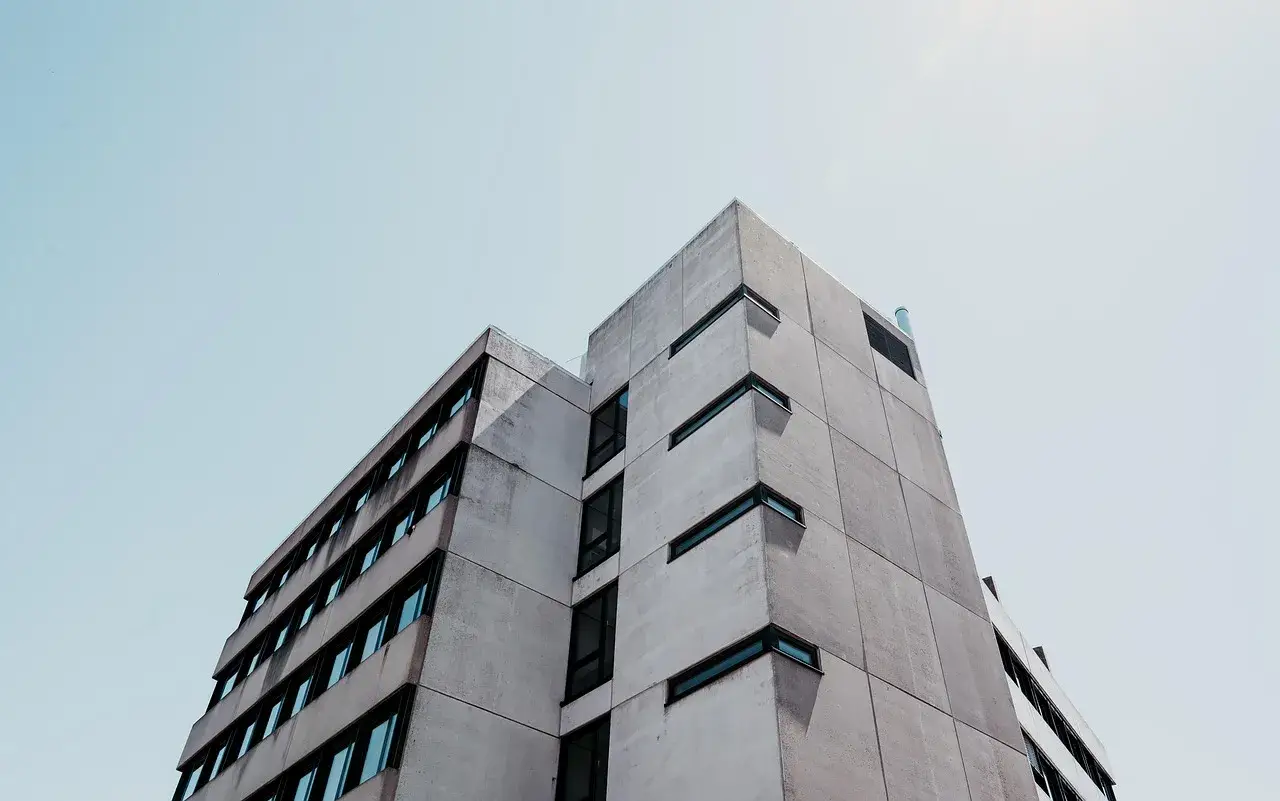 Betonowy budynek o geometrycznej bryle, z rzędami okien. Ta kategoria obiektu budowlanego dominuje w kadrze.