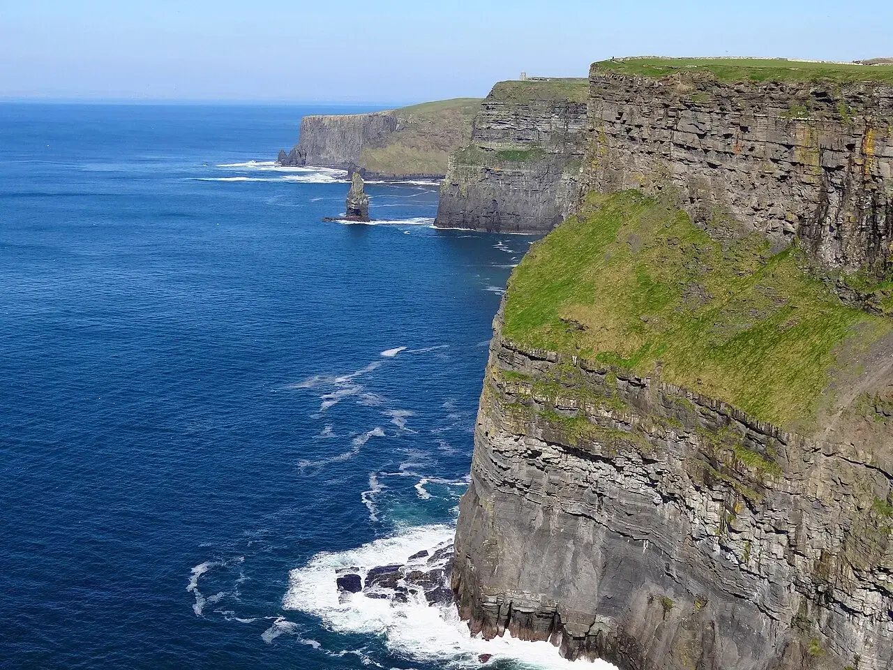 Majestatyczne klify Irlandii wznoszą się nad błękitnym oceanem. Zielone zbocza kontrastują z szarymi skałami, tworząc zapierający dech w piersiach krajobraz.
