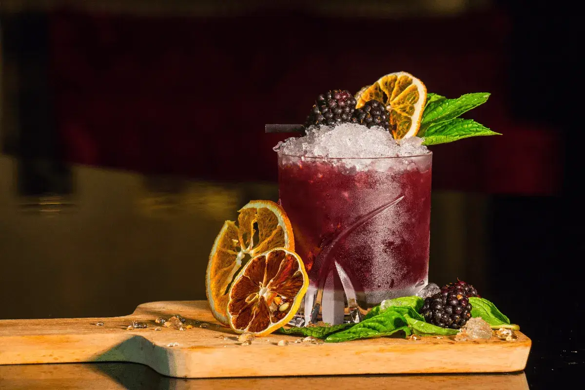 Cocktail rosso con frutti di bosco, arancia essiccata e menta, perfetto per un aperitivo a Riccione.