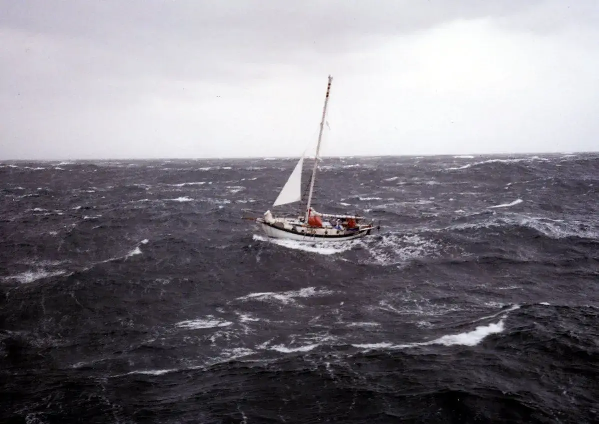 Un voilier affronte une mer agitée, sa voile blanche tendue. La mise à la cape est une manœuvre de survie face aux éléments déchaînés.