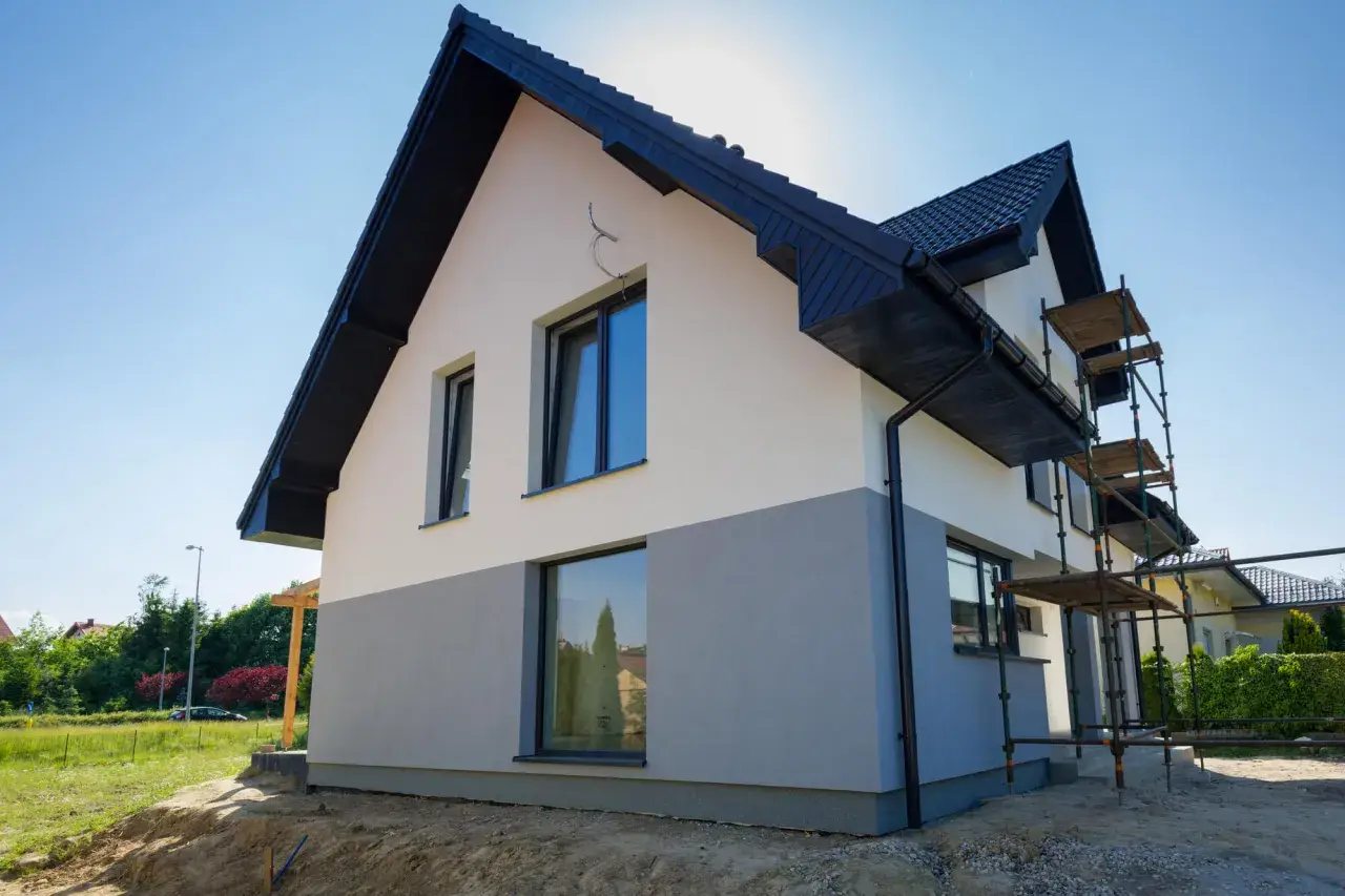 Nowy dom w trakcie budowy, z dwukolorową elewacją i rusztowaniami. Czekamy na wykończenie, by podziwiać efekt końcowy.