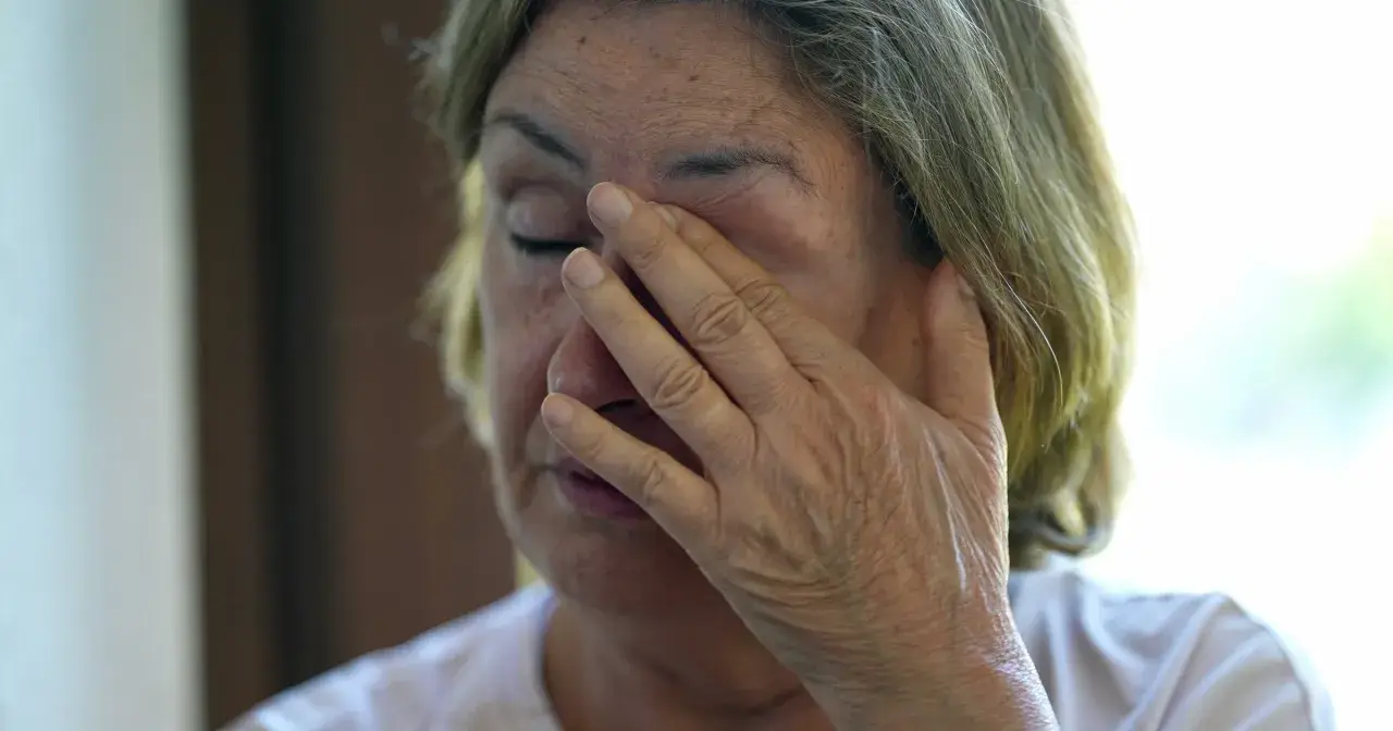 Starsza kobieta zasłaniająca oko dłonią.