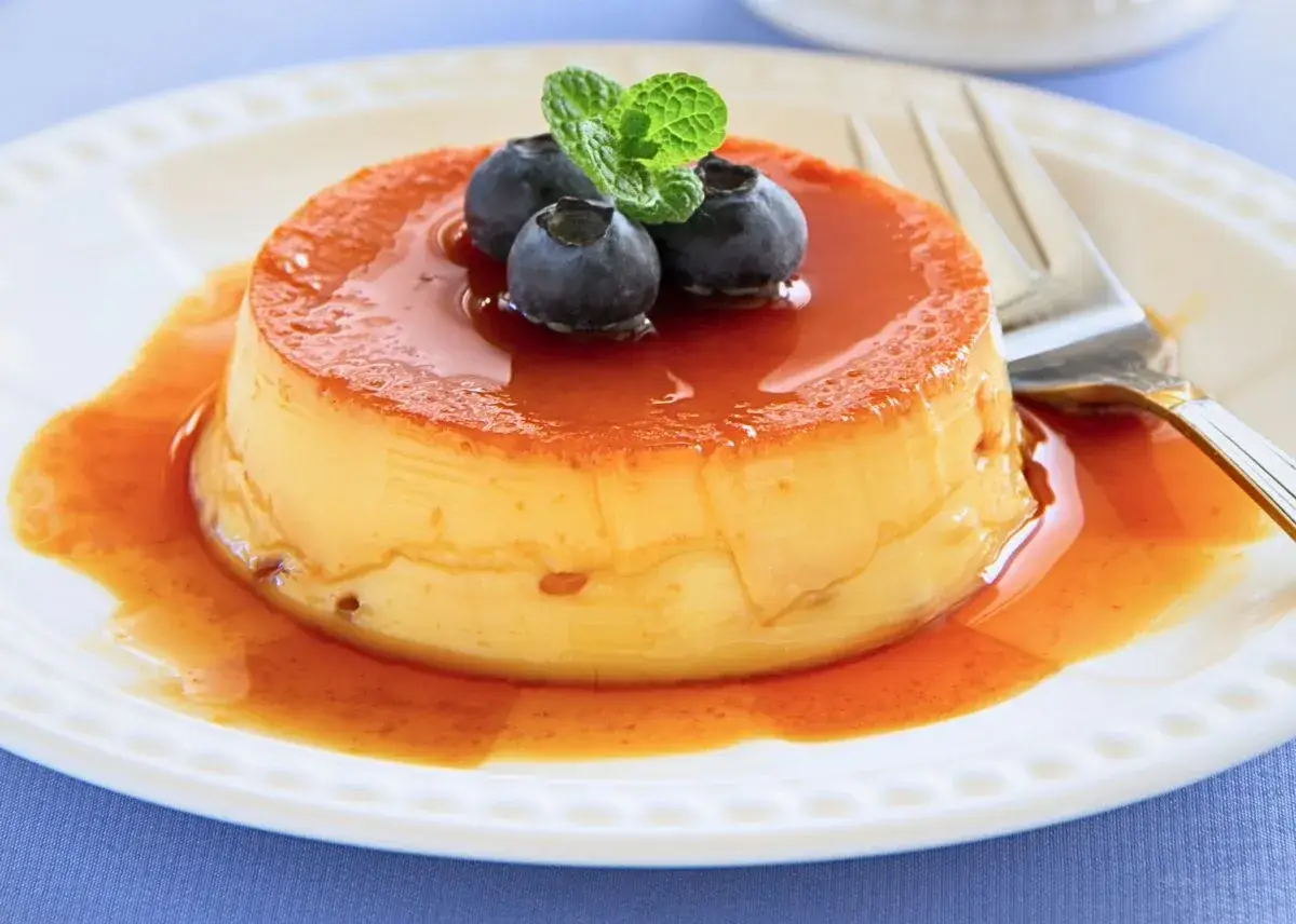 Delicioso flan de queso con cuajada, cubierto de caramelo líquido y adornado con arándanos y menta.